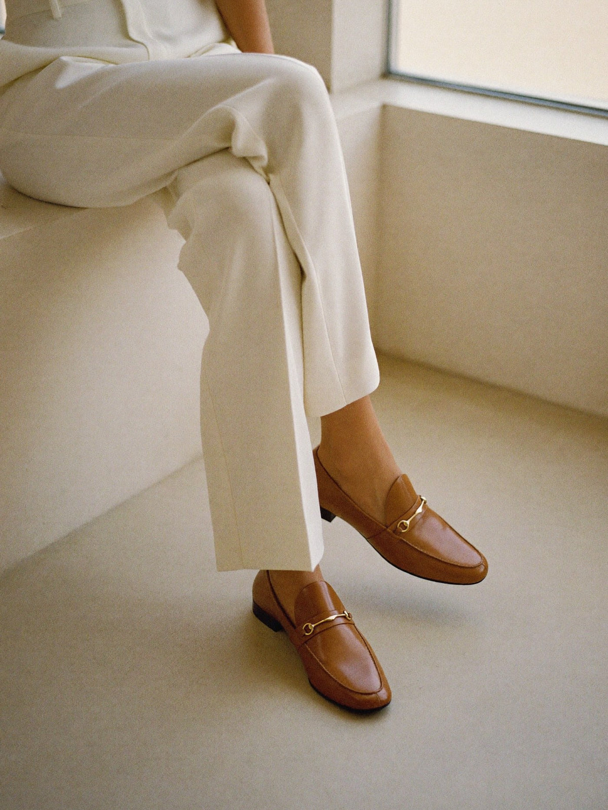 Tan leather loafers worn with ivory tailored trousers