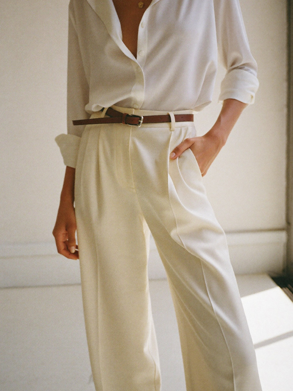 Woman in cream high-waisted wide-leg trousers and an ivory silk shirt