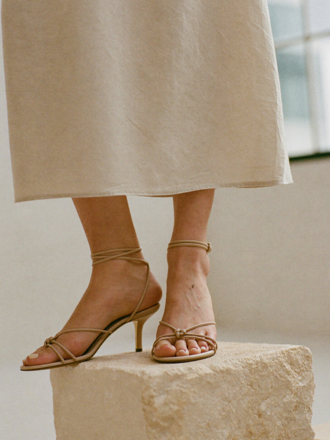 Strappy nude leather heeled sandals worn with a linen skirt