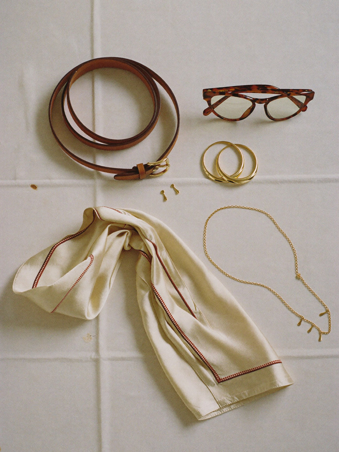 Flat lay of a leather belt, gold hoops, silk scarf and sunglasses