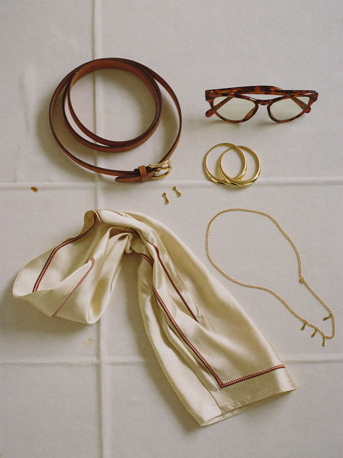 Flat lay of a leather belt, gold hoops, silk scarf and sunglasses