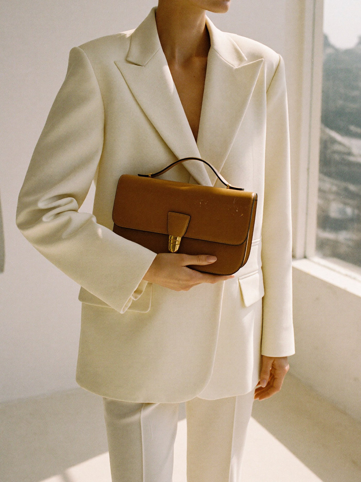 Woman in a cream blazer holding a tan leather bag