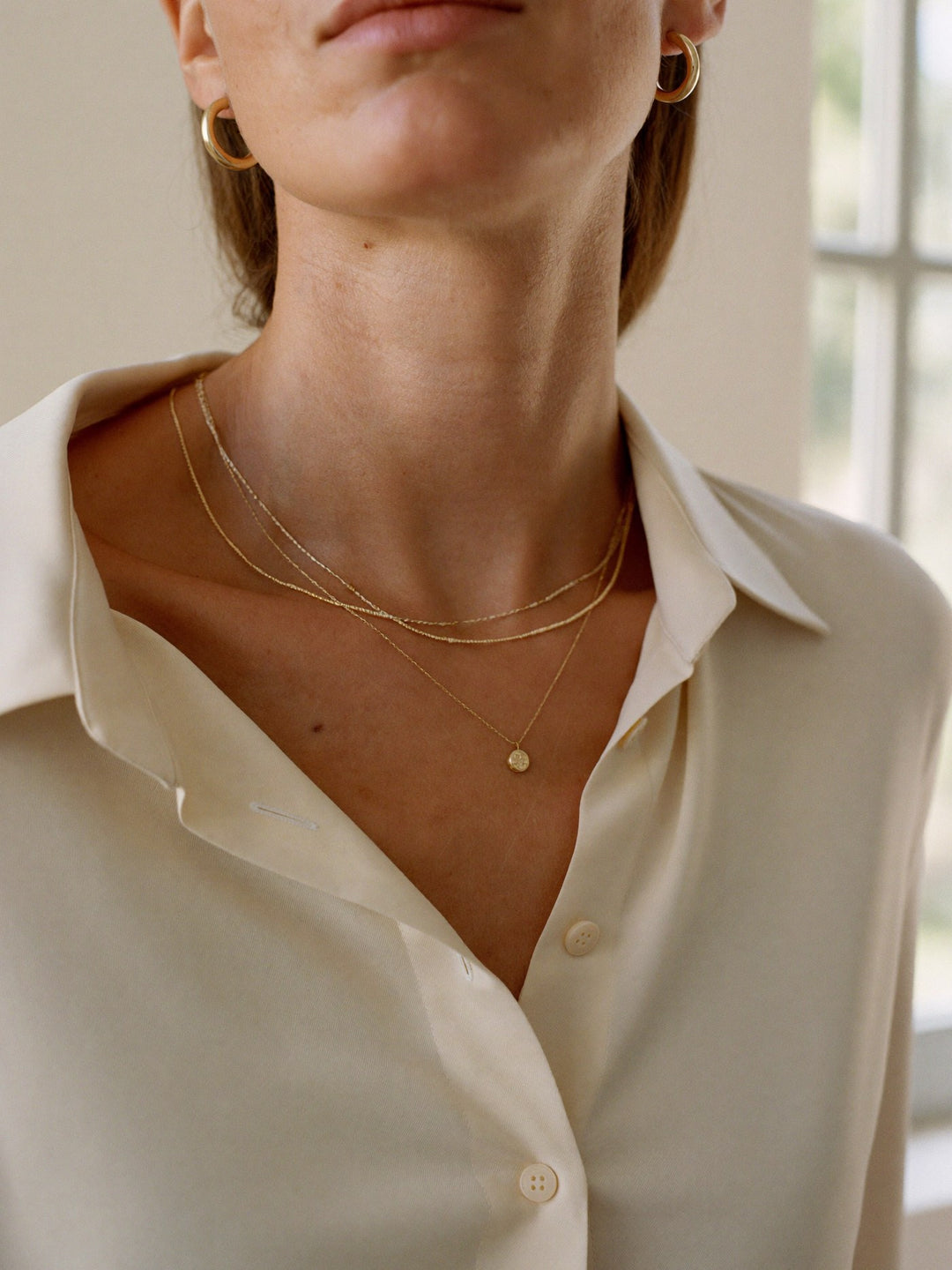Layered fine gold necklaces worn with a cream silk blouse