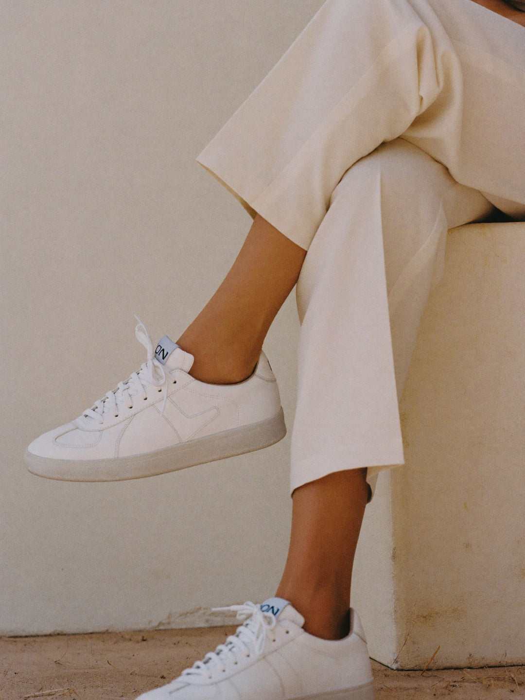 White leather sneakers worn with cream cropped trousers